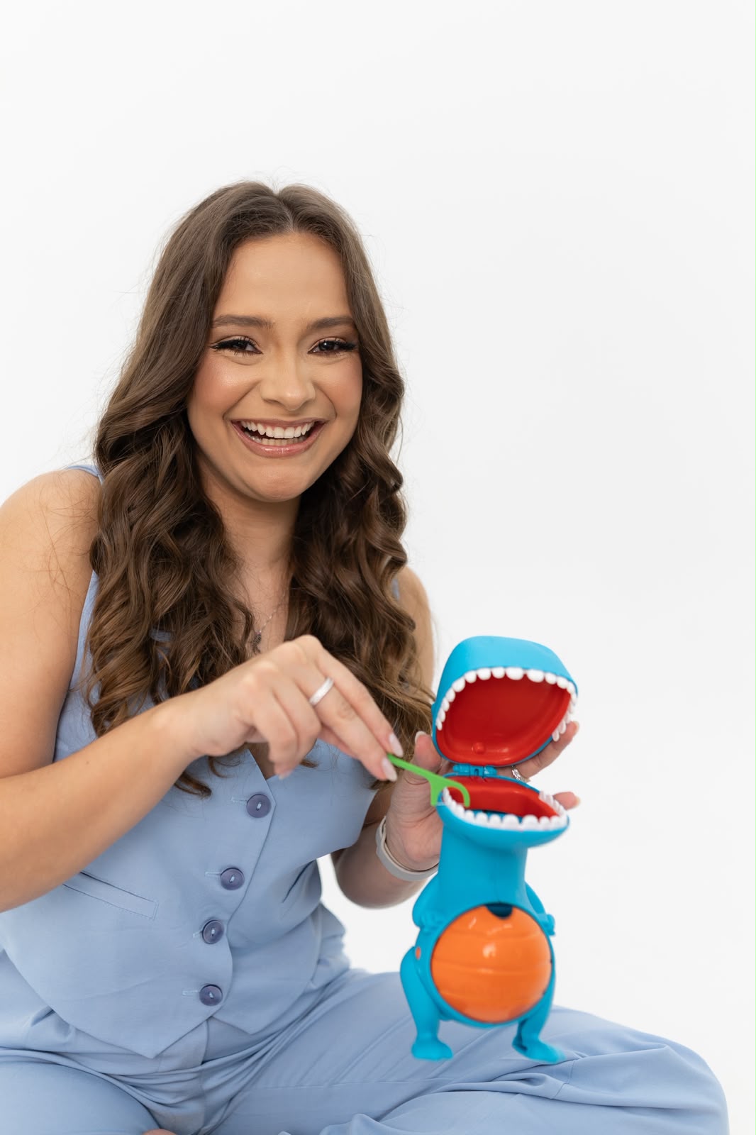 Dra. Giulianna Barreto sorrindo, segurando um brinquedo de dinossauro usado para deixar as crianças à vontade no consultório