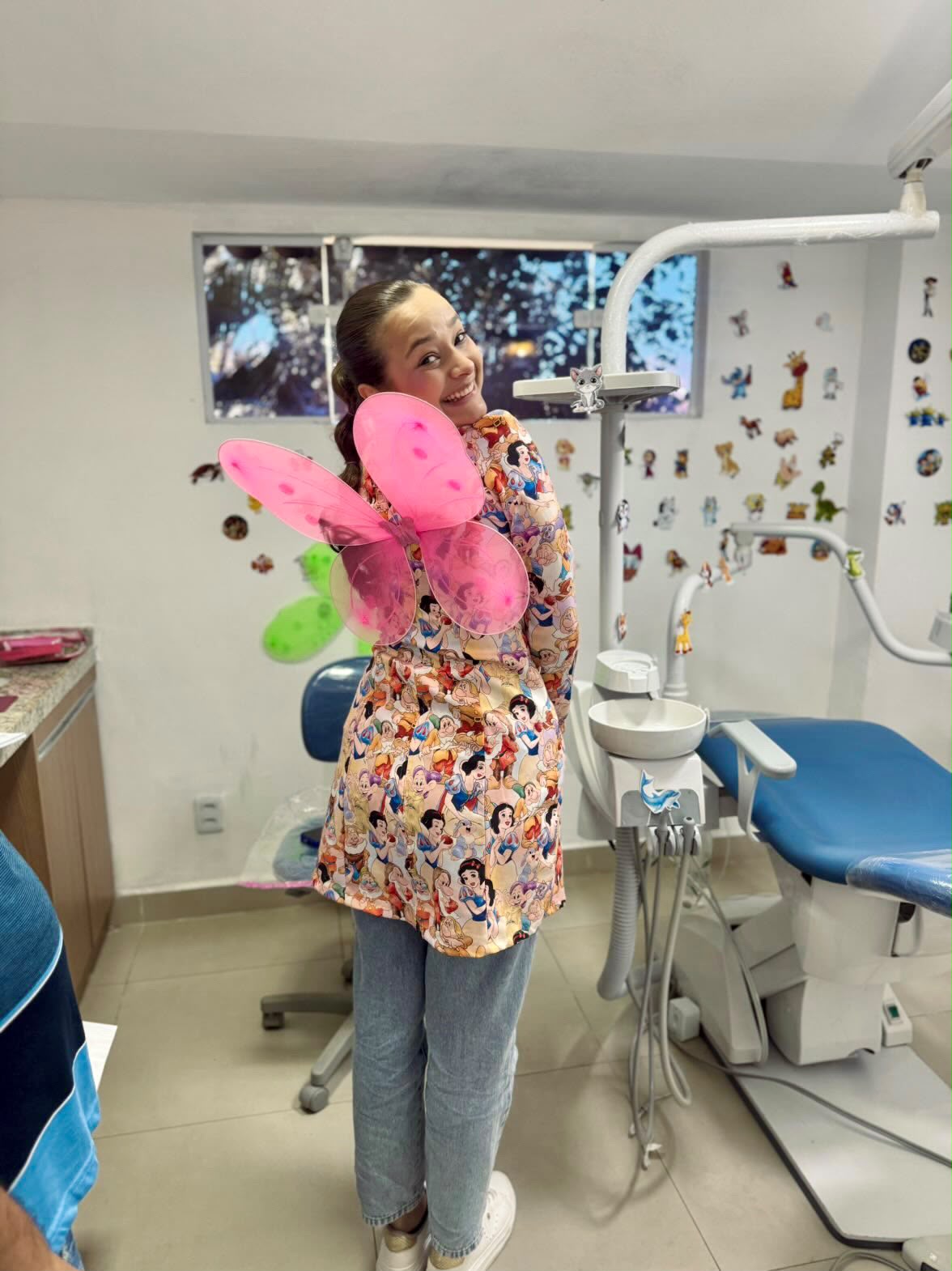 Dra. Giulianna Barreto usando asas de borboleta cor-de-rosa no consultório, em referência à Fadinha do Dente