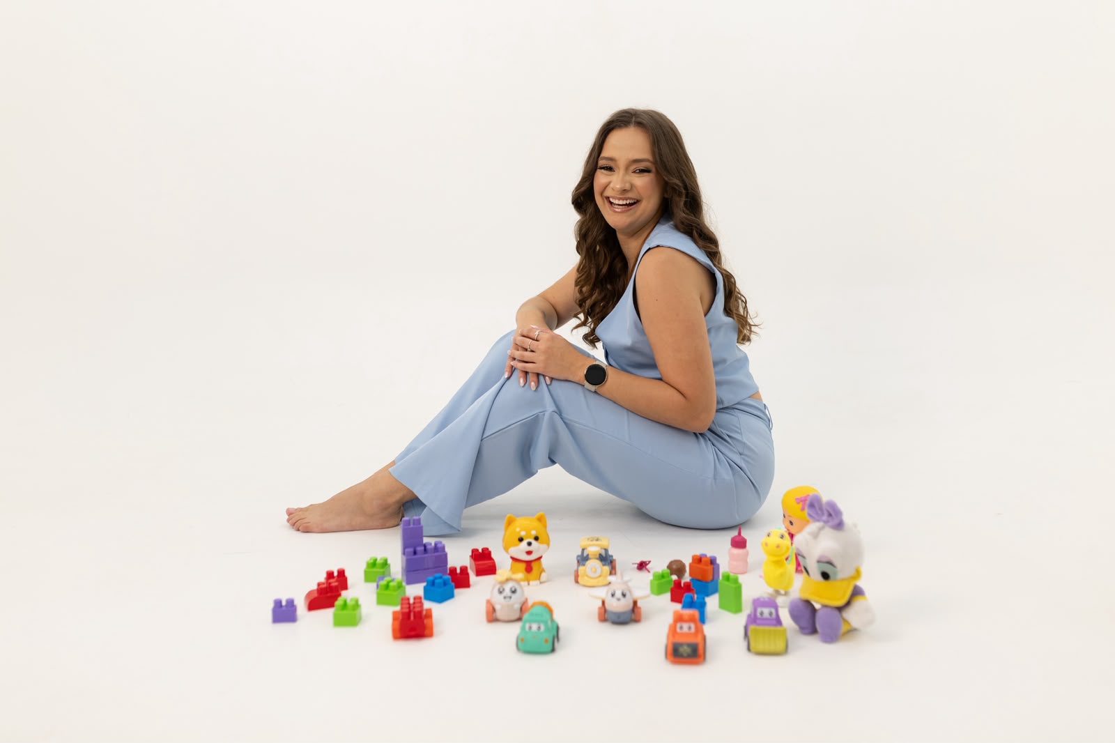 Dra. Giulianna Barreto sentada e sorrindo, cercada de brinquedos coloridos usados no consultório