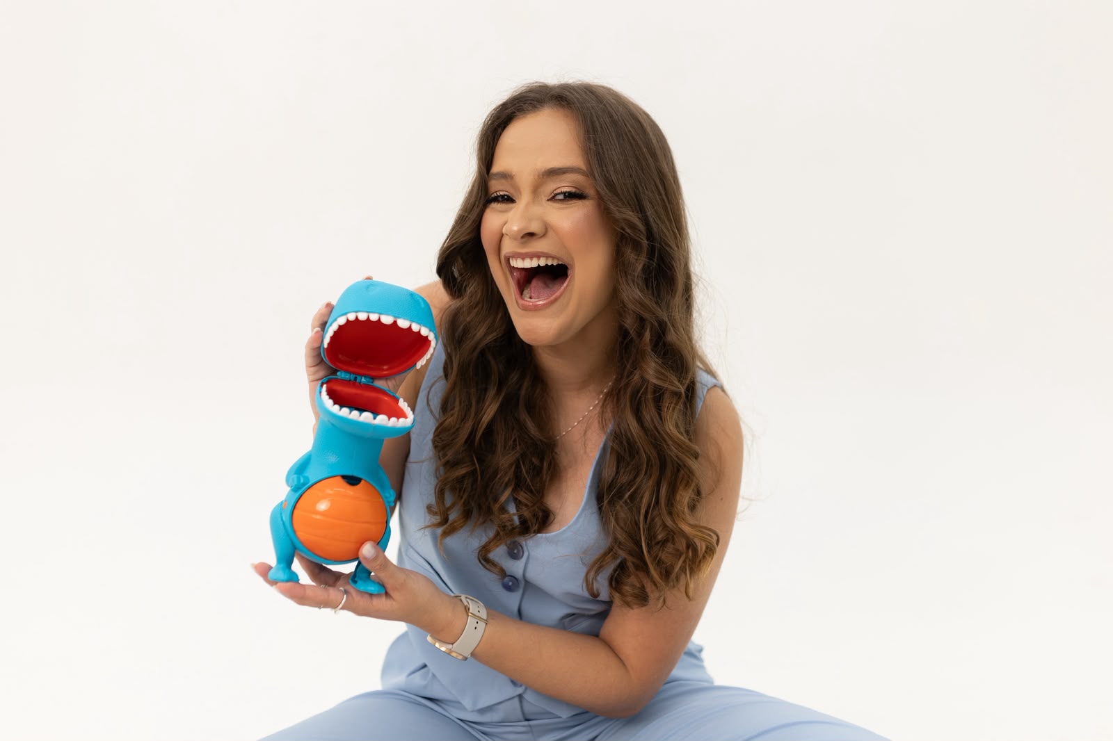 Dra. Giulianna Barreto rindo, segurando um brinquedo de dinossauro usado para acolher crianças com mais sensibilidade ao atendimento
