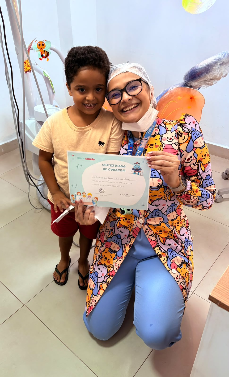 Menino sorrindo ao lado da Dra. Giulianna Barreto, segurando seu Certificado de Coragem