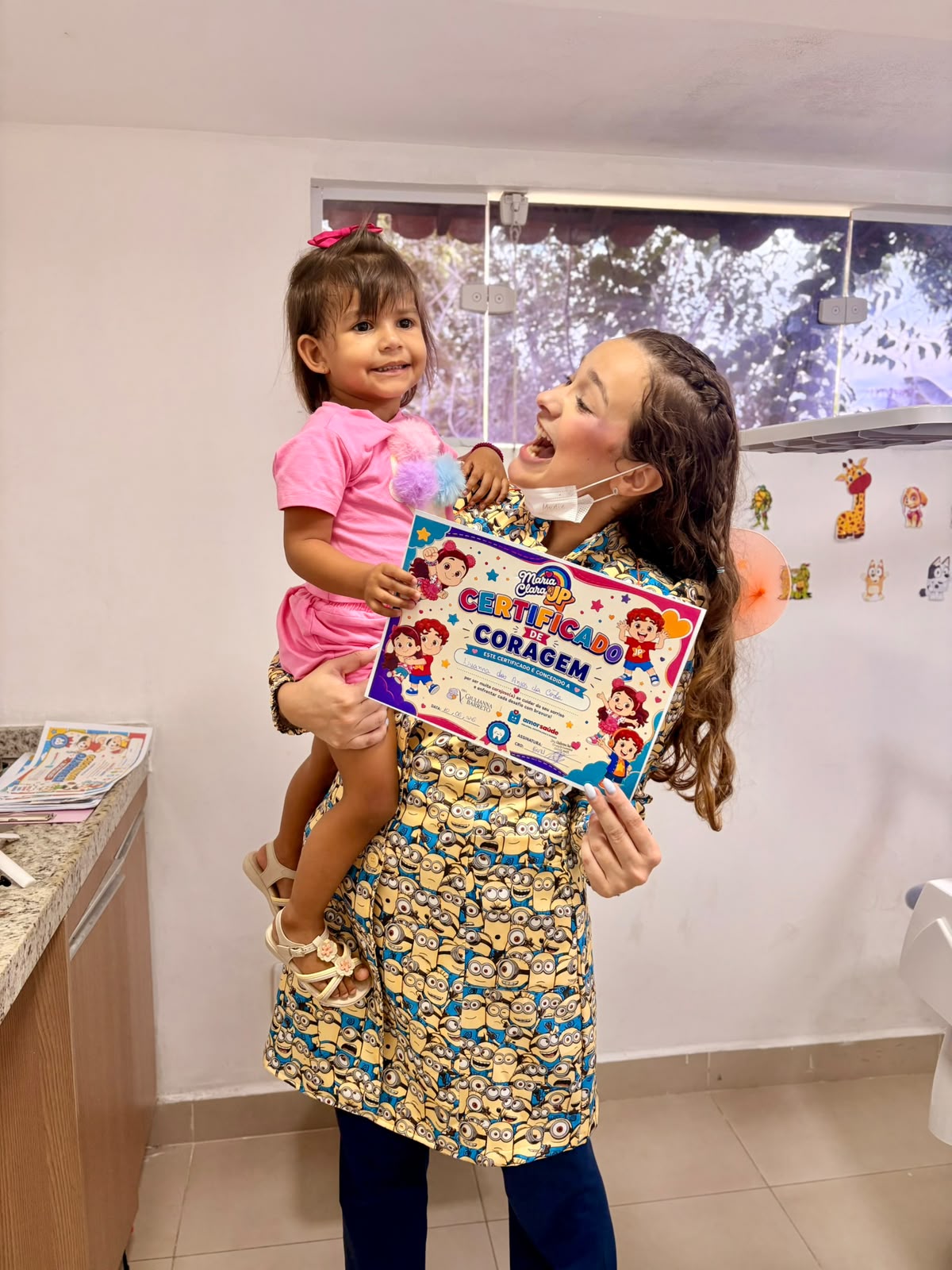 Dra. Giulianna Barreto segurando uma criança pequena que exibe seu Certificado de Coragem