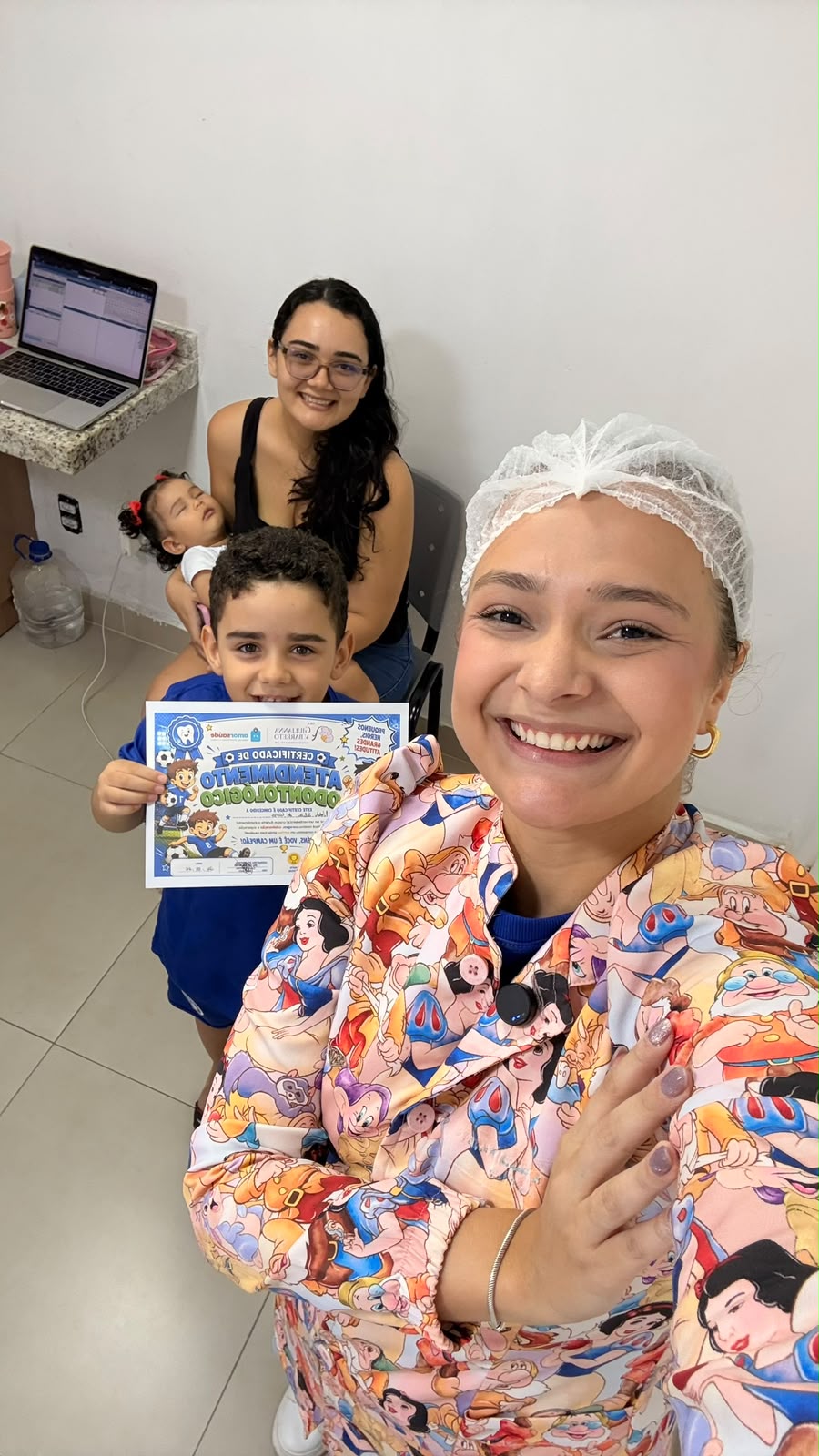 Dra. Giulianna Barreto com uma família e duas crianças, segurando o certificado de atendimento odontológico